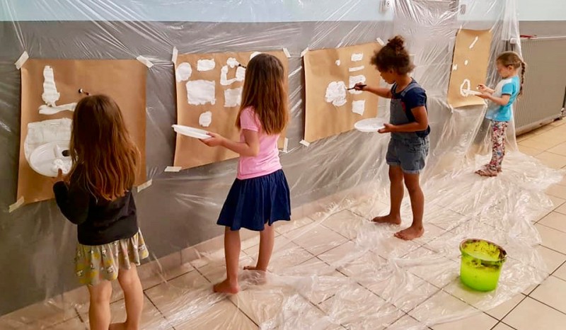 Petites filles peintent sur des grandes feuilles de papier attachés au mur