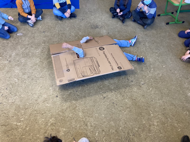 een kind ligt verscholen onder een stuk karton op de grond