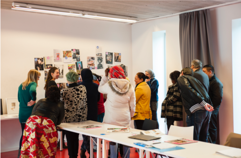 Een jonge vrouw toont verschillende kunstwerk aan een diverse groep vrouwen