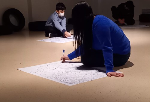 Une fille assise dessine au marqueur sur une grande feuille blanche.