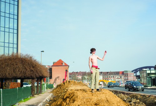 Jongen in ontbloot bovenlijf imiteert vrouwe justitia op een berg zand